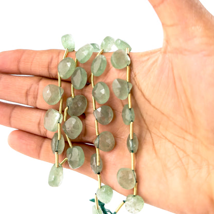 A person holds Strawberry Quartz briolette beads, showing their faceted design and warm green colour.