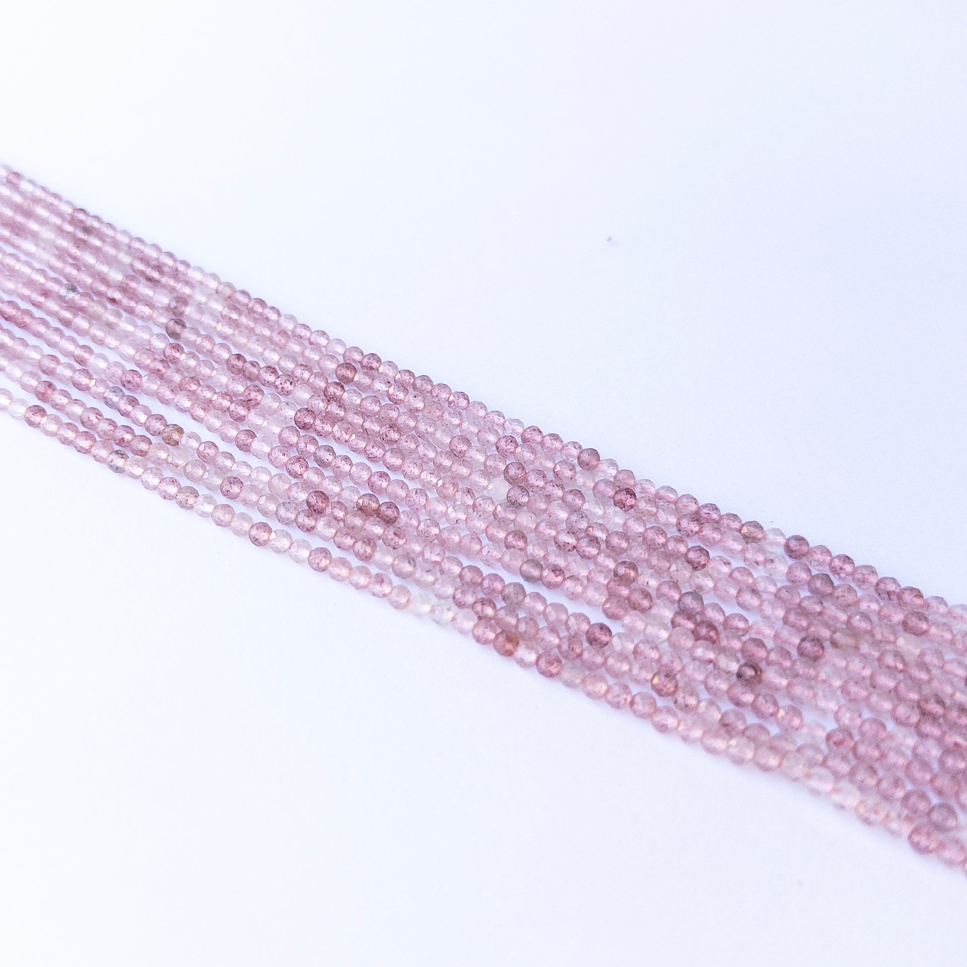 Premium Strawberry Quartz gemstone beads in faceted rondelle cut arranged in strands, showcasing natural pink inclusions for jewellery designers.