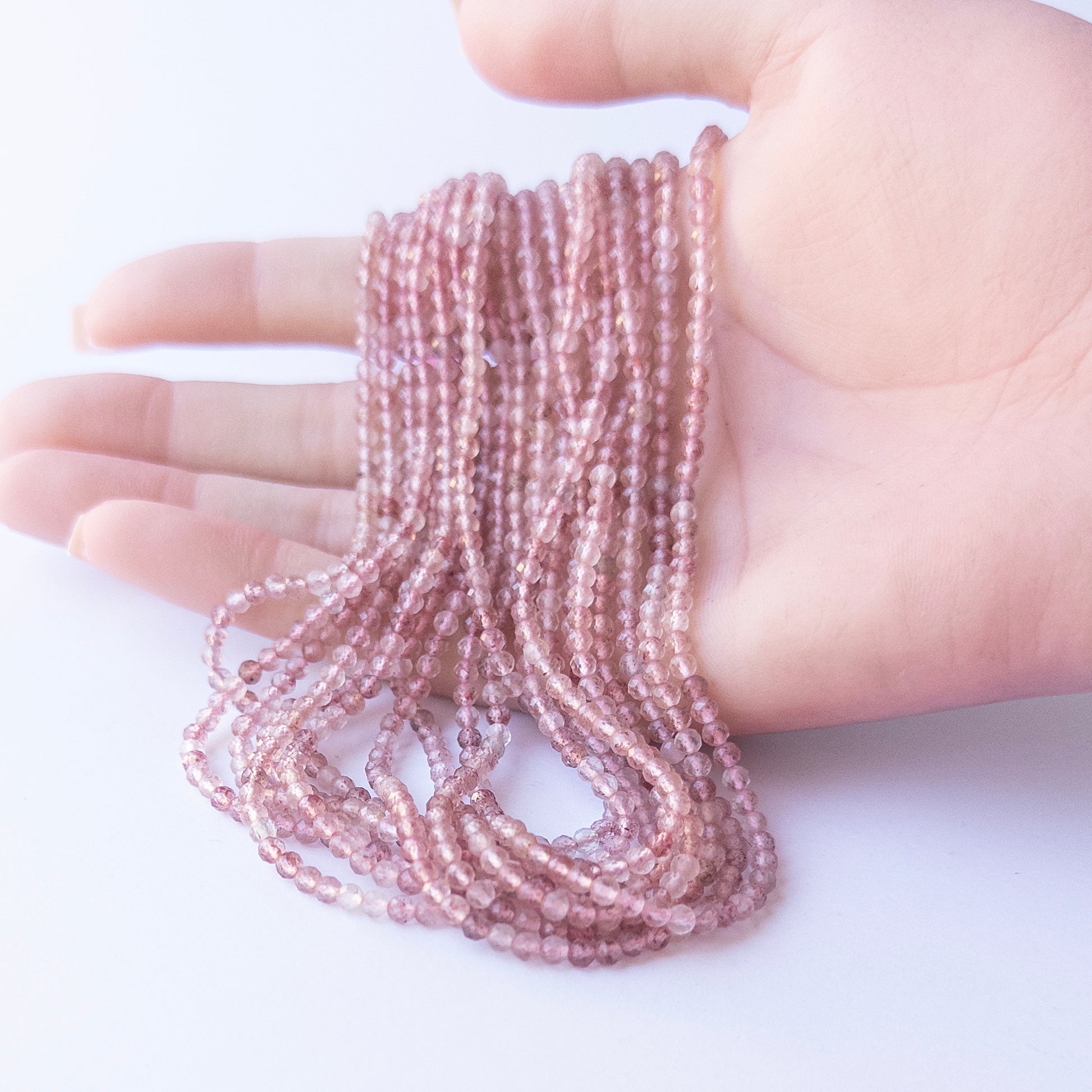 A person holds delicate strands of Strawberry Quartz beads, showcasing their faceted rondelle design.