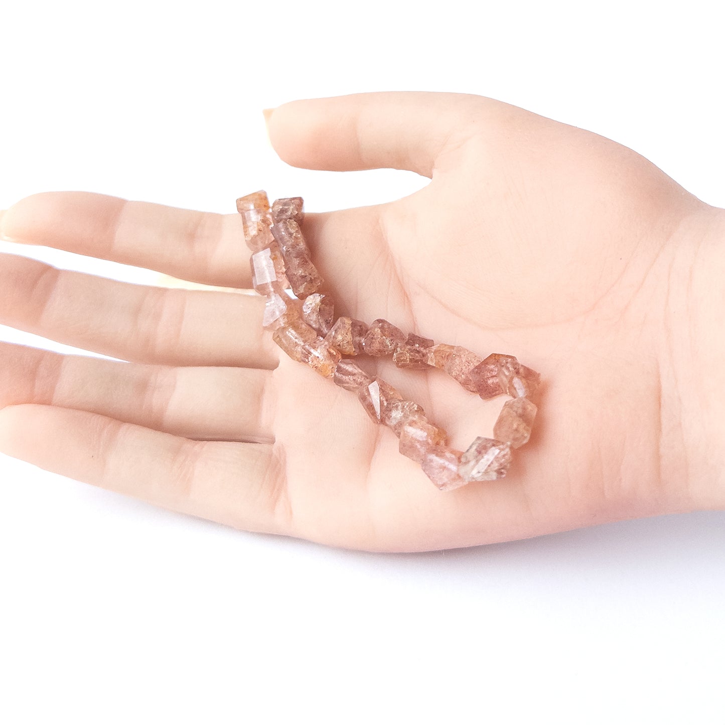 A person holds delicate strands of Strawberry Quartz beads, showcasing their faceted tumble design.