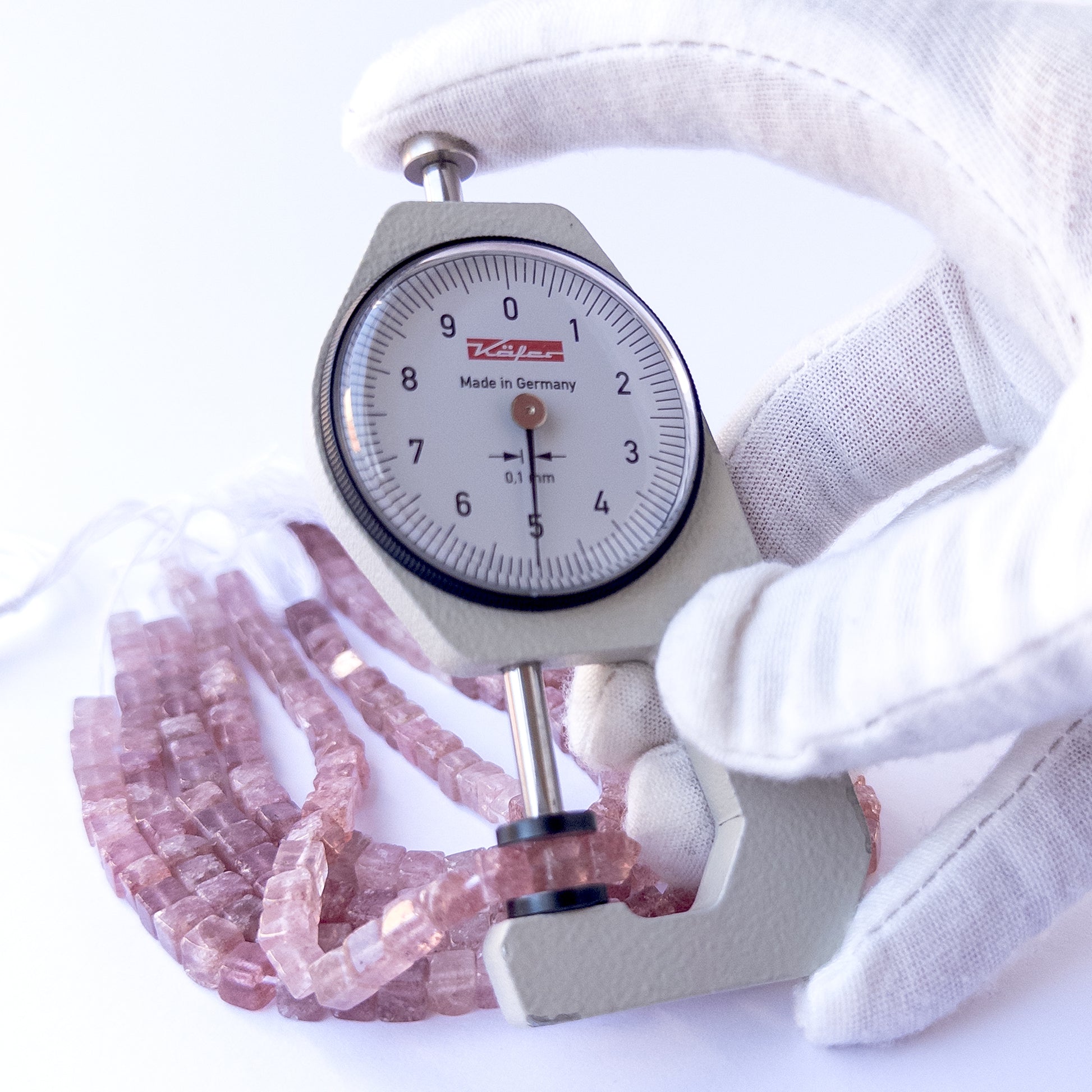 A dial gauge measures the Strawberry Quartz smooth cube 5–5.3mm gemstone.