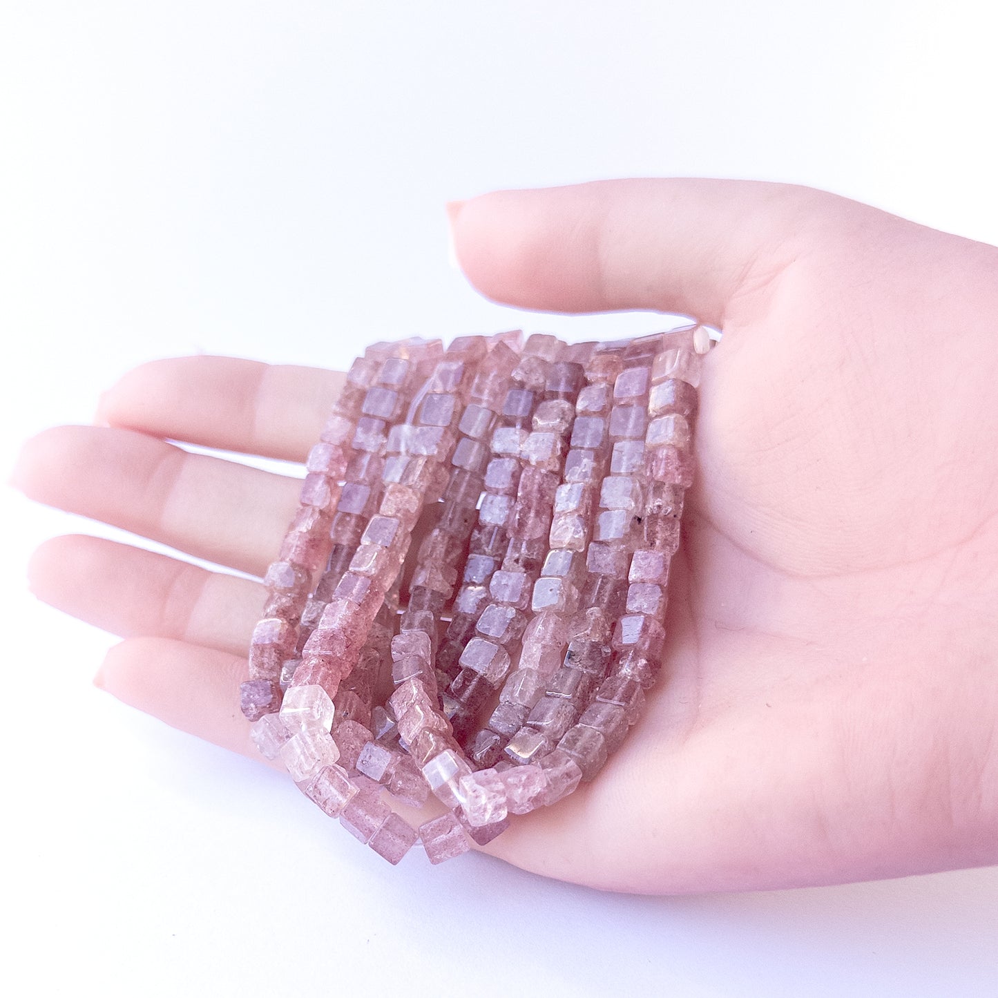 A person holds delicate strands of Strawberry Quartz beads, showcasing their smooth cube design.