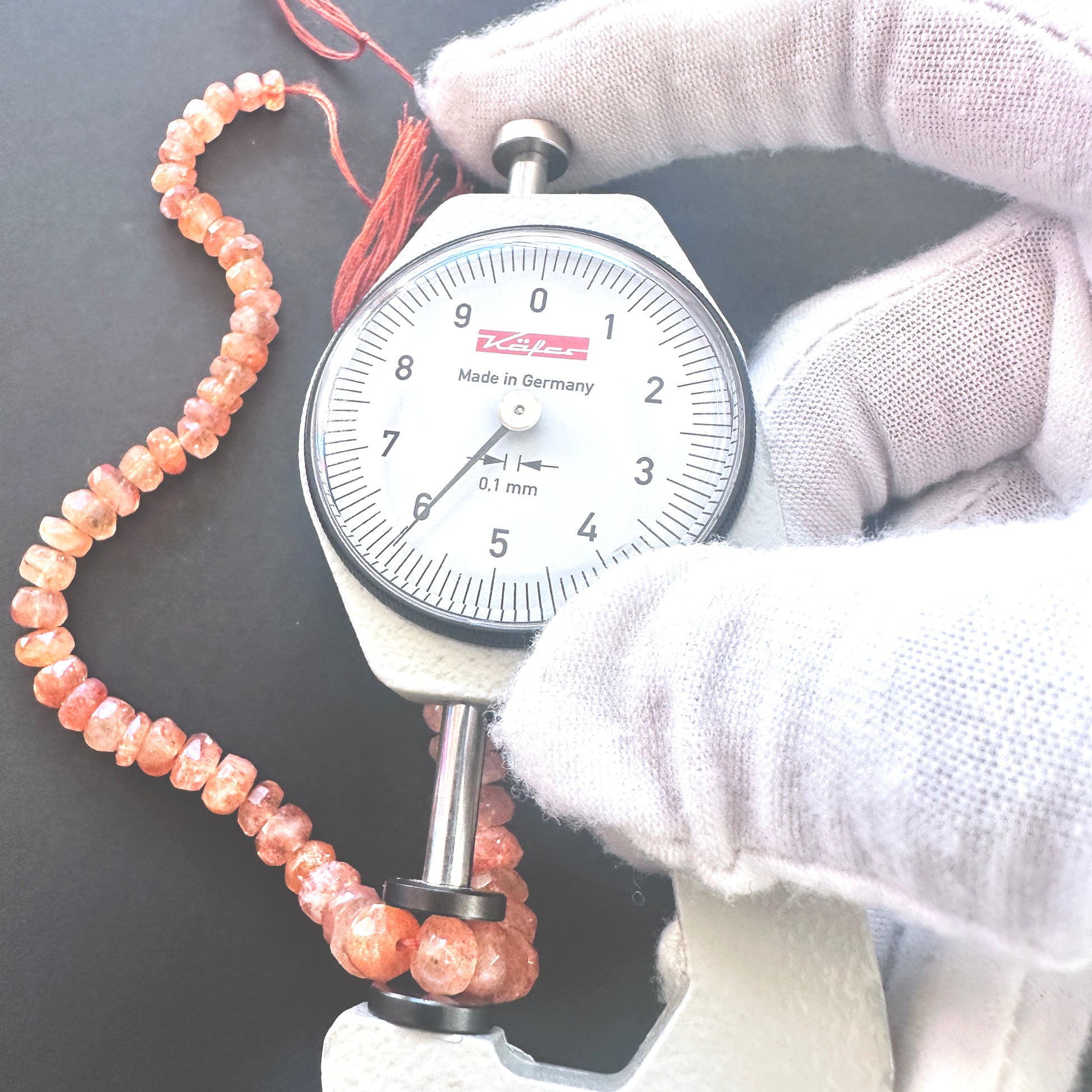 A dial gauge measures the Sunstone faceted rondelle 4.5-7mm gemstone.