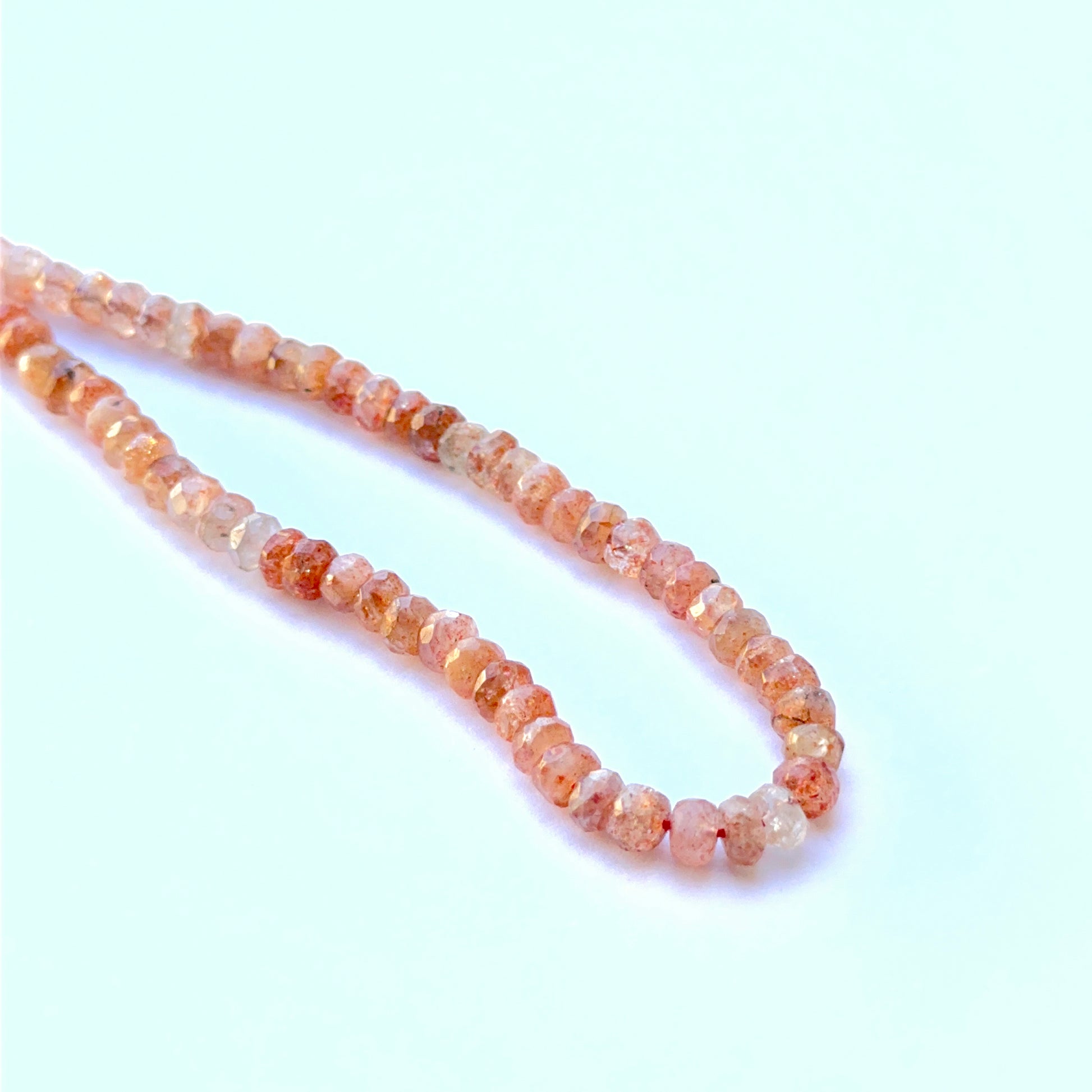Sunstone faceted rondelle natural gemstone beads with warm peach sparkle arranged on a 20cm strand for handmade jewellery components.