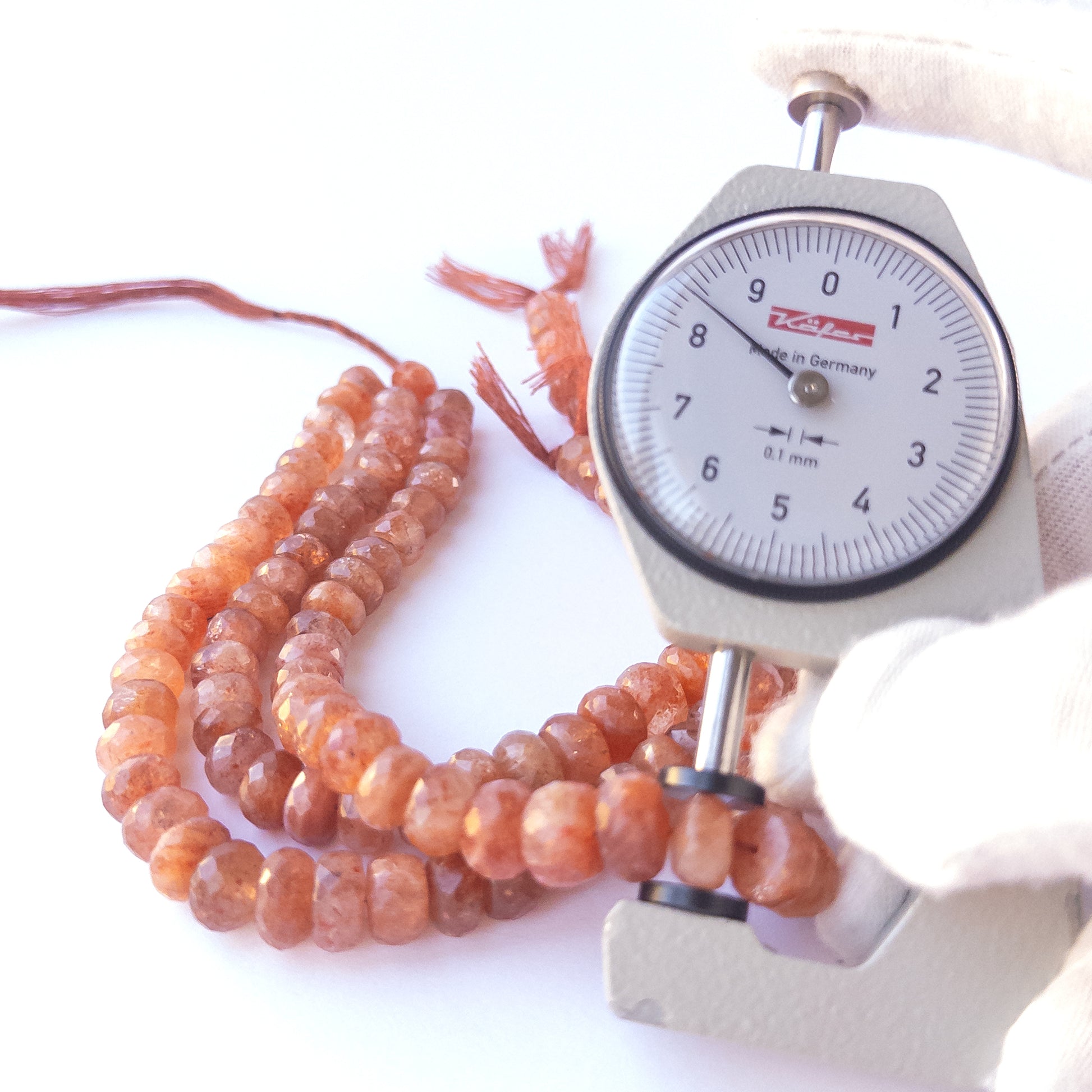 A dial gauge measures the Sunstone faceted rondelle 7–9.5mm gemstone.