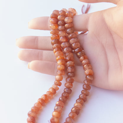 A person holds delicate strands of Sunstone beads, showcasing their faceted rondelle design.