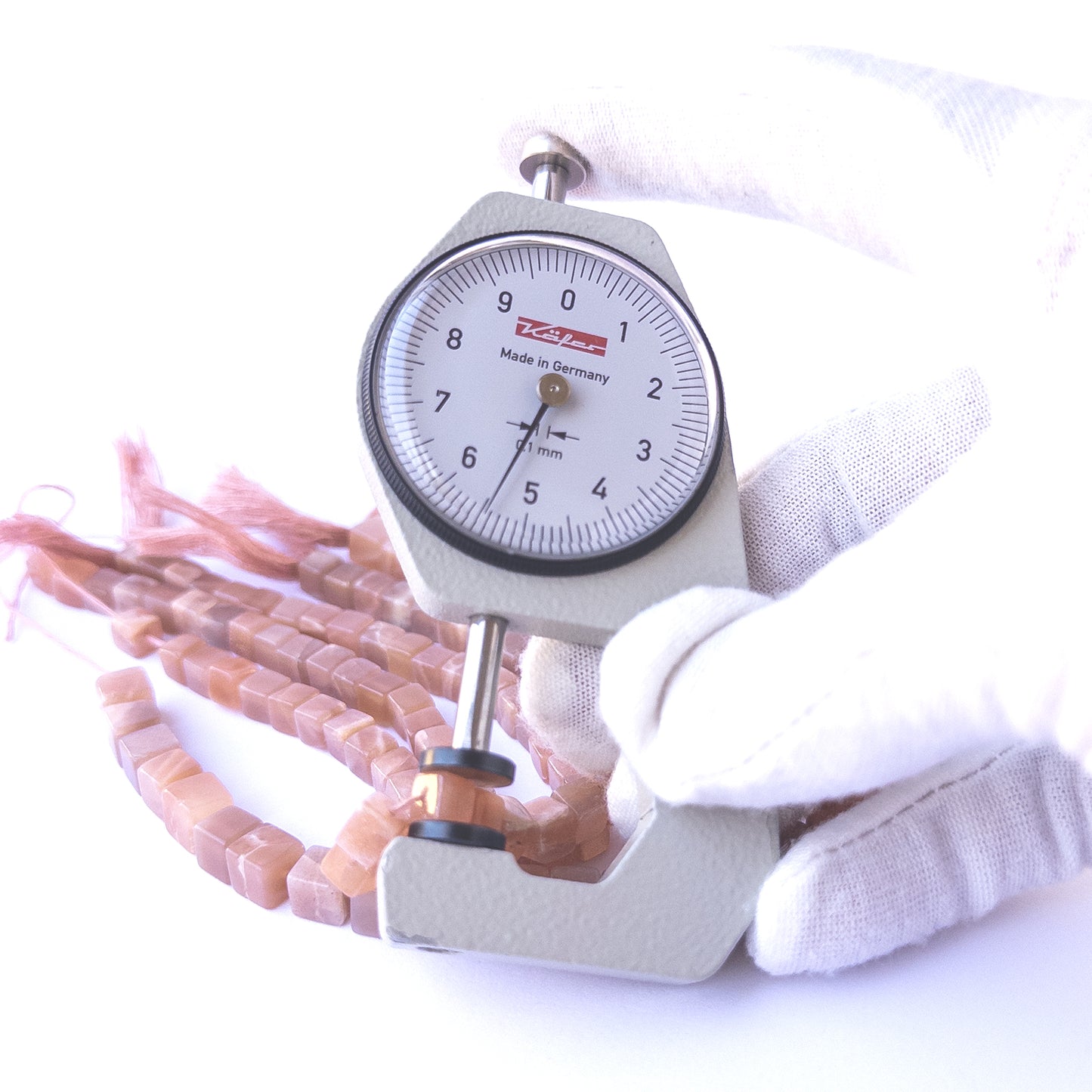 A dial gauge measures the Sunstone smooth cube 5–7mm gemstone.