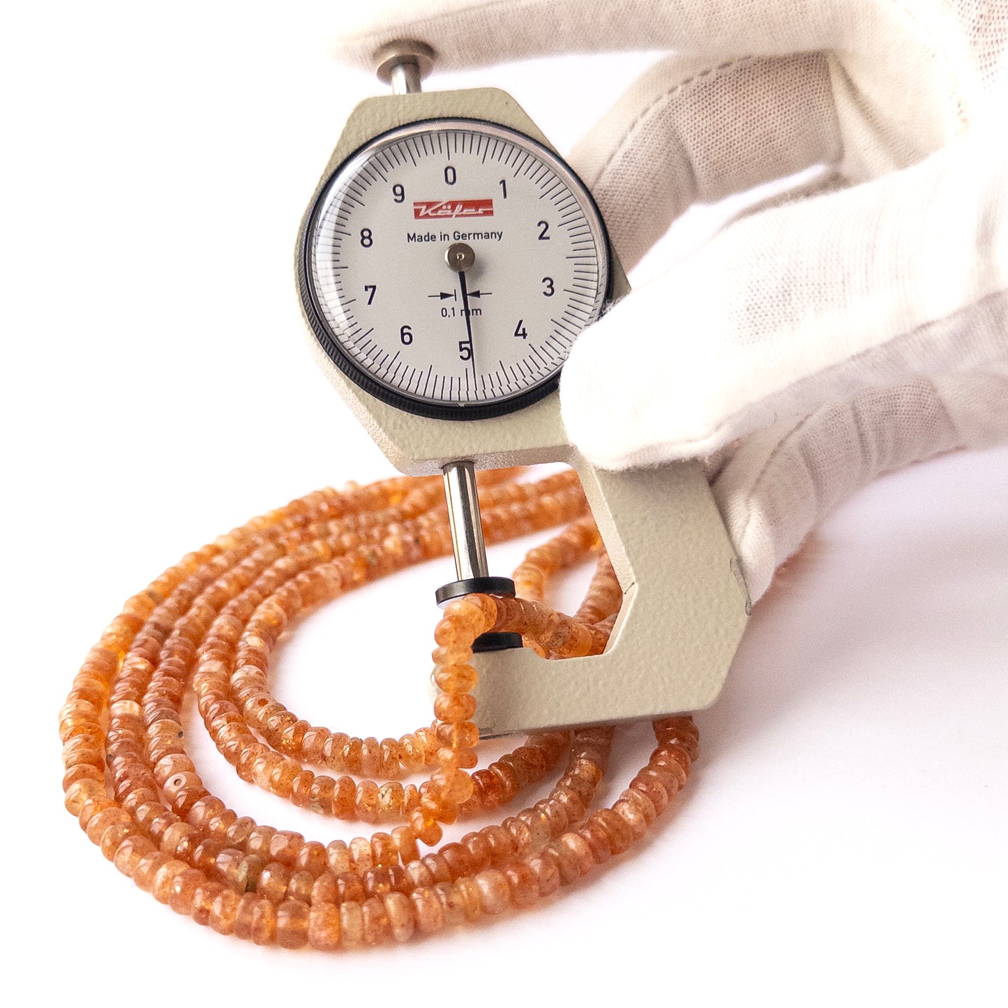 A dial gauge measures the Sunstone smooth rondelle 4.9–5.2mm gemstone bead.