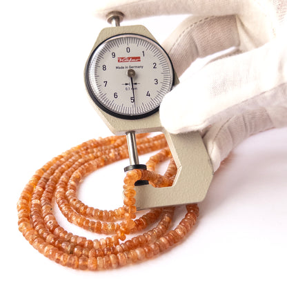 A dial gauge measures the Sunstone smooth rondelle 4.9–5.2mm gemstone bead.