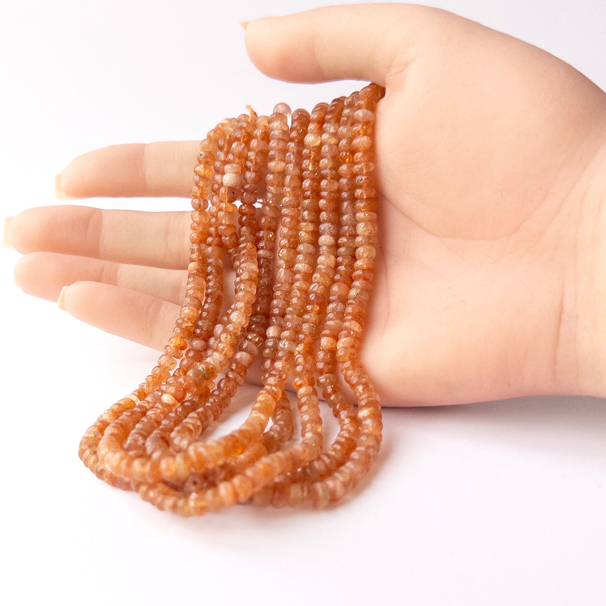 A person holds delicate strands of Sunstone beads, showcasing their smooth rondelle design.