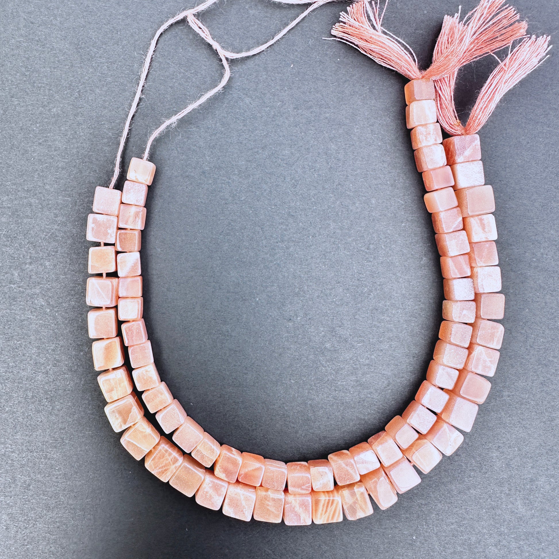Close-up of Sunstone smooth square beads with warm golden-orange tones and polished finish.