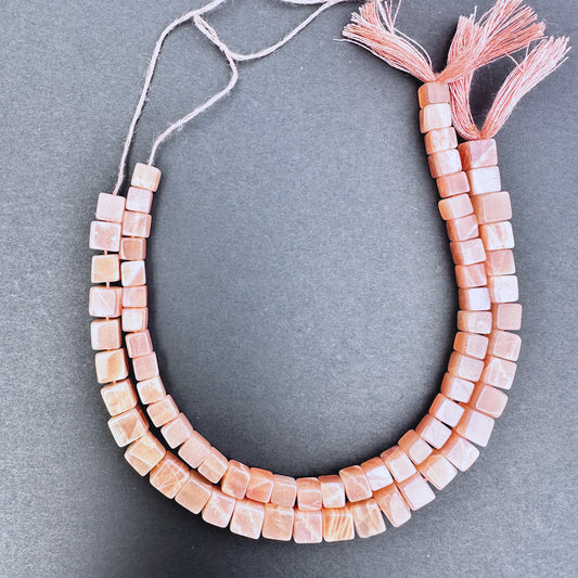 Close-up of Sunstone smooth square beads with warm golden-orange tones and polished finish.