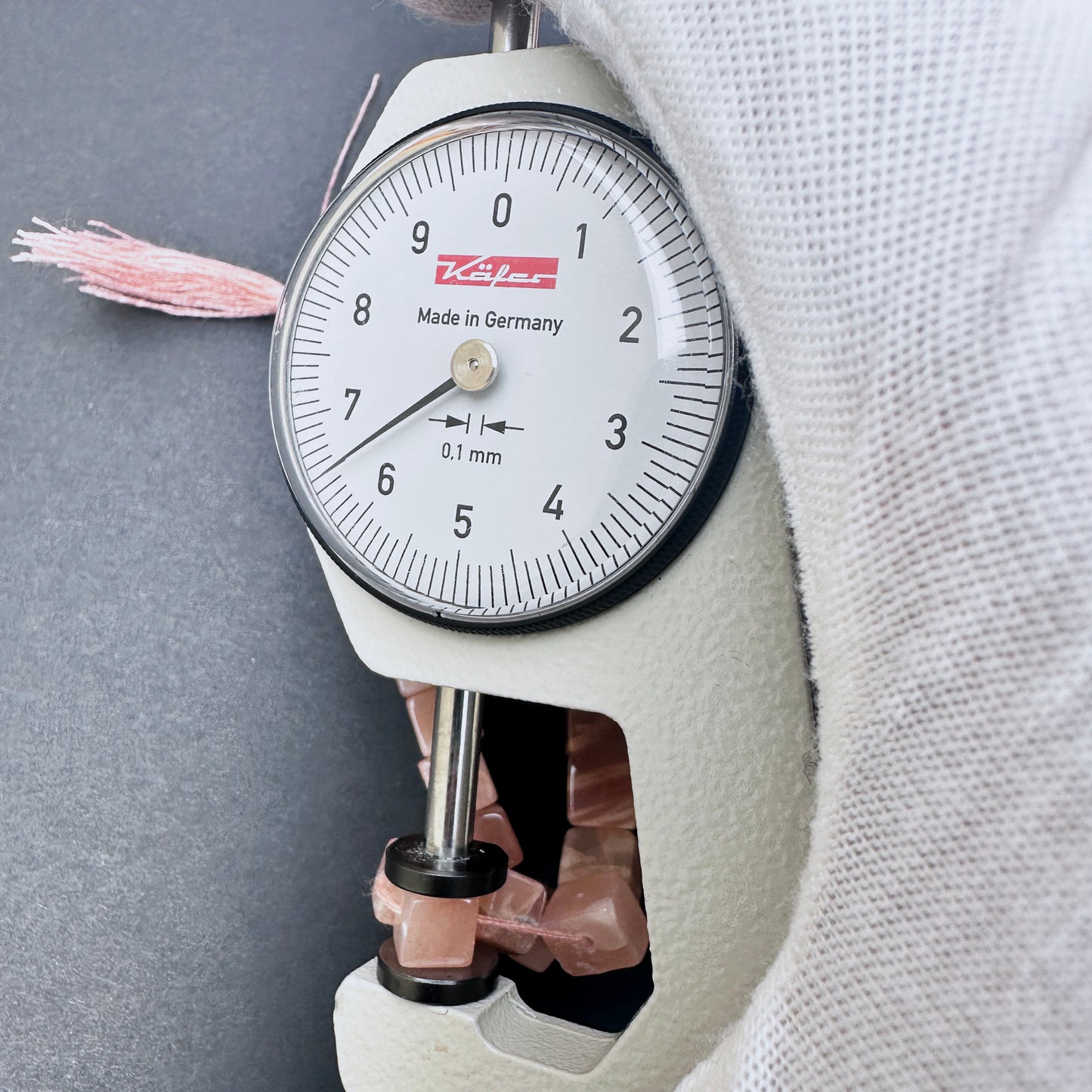 A dial gauge measures the Sunstone smooth square 5.5-6mm gemstone.