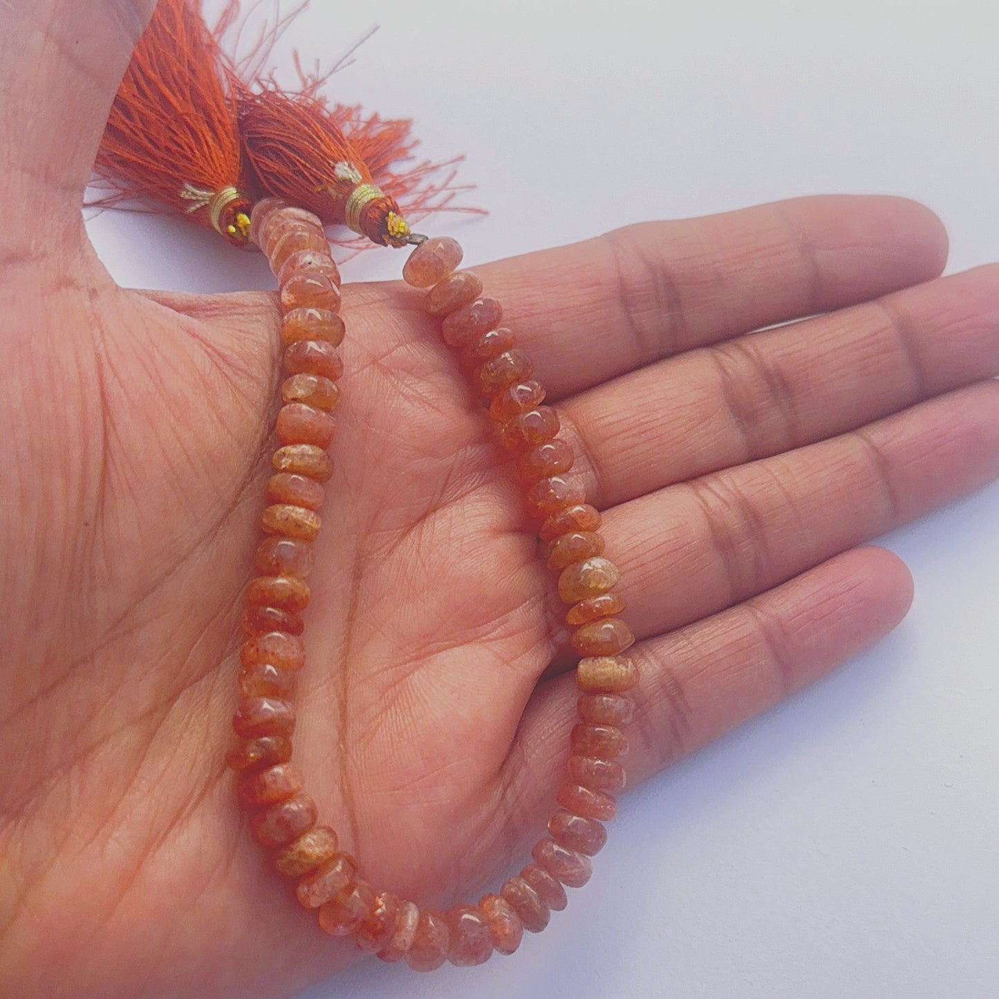 A person holds delicate strands of sunstone beads, showcasing their smooth design