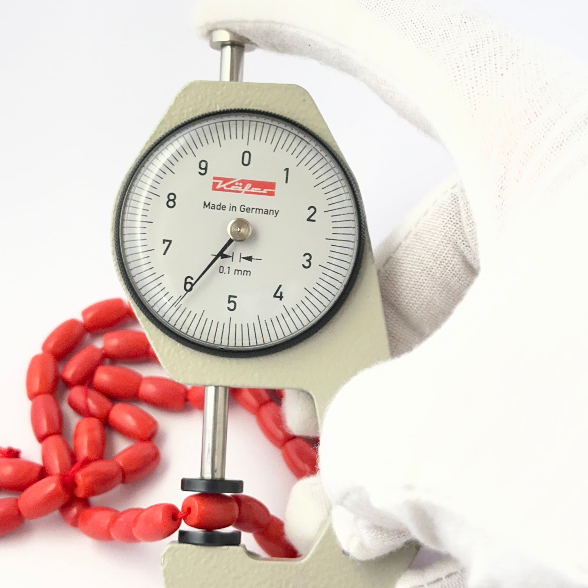 A dial gauge measures the Taiwan Coral oval 8.5mm x 6mm gemstone.