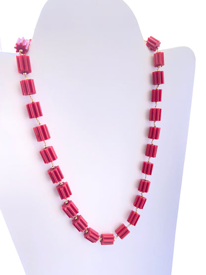Close‑up of faceted coral cylinder beads arranged on a polished necklace.