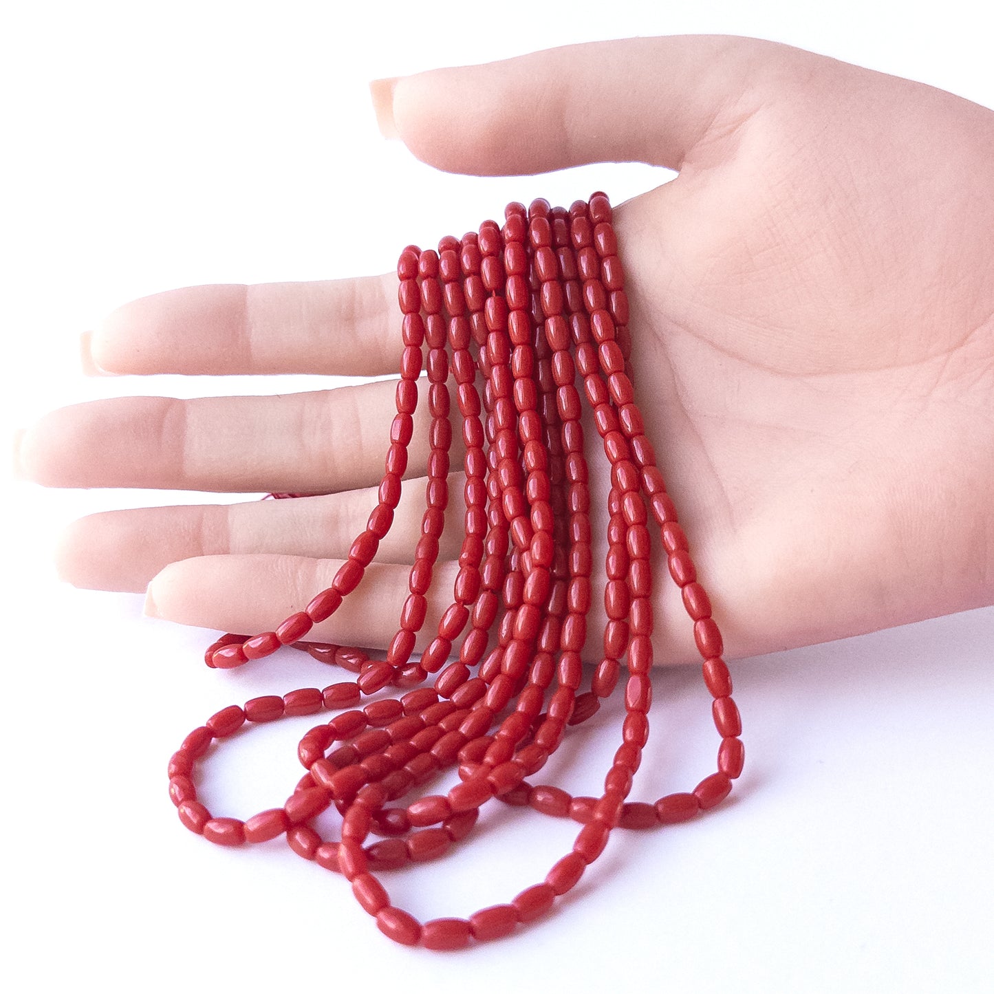 A person holds delicate strands of Taiwan Coral beads, showcasing their smooth drum design.