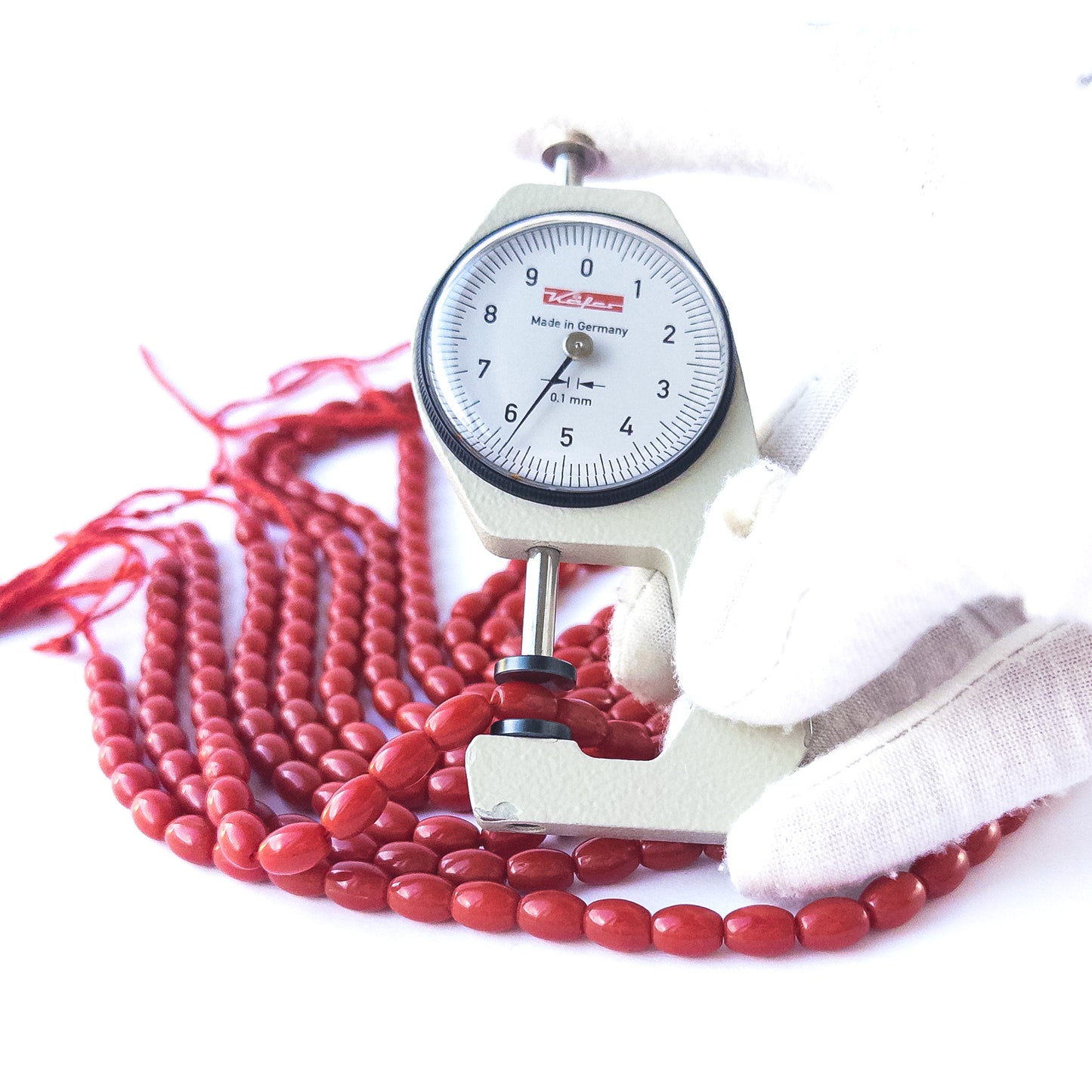 A dial gauge measures the Taiwan Coral smooth drum 8mm × 5.8mm gemstone.