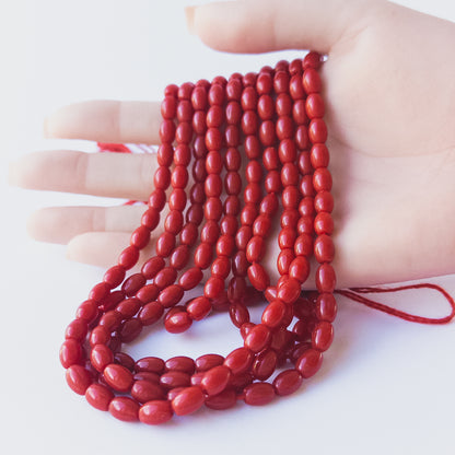 A person holds delicate strands of Taiwan Coral beads, showcasing their smooth drum design.