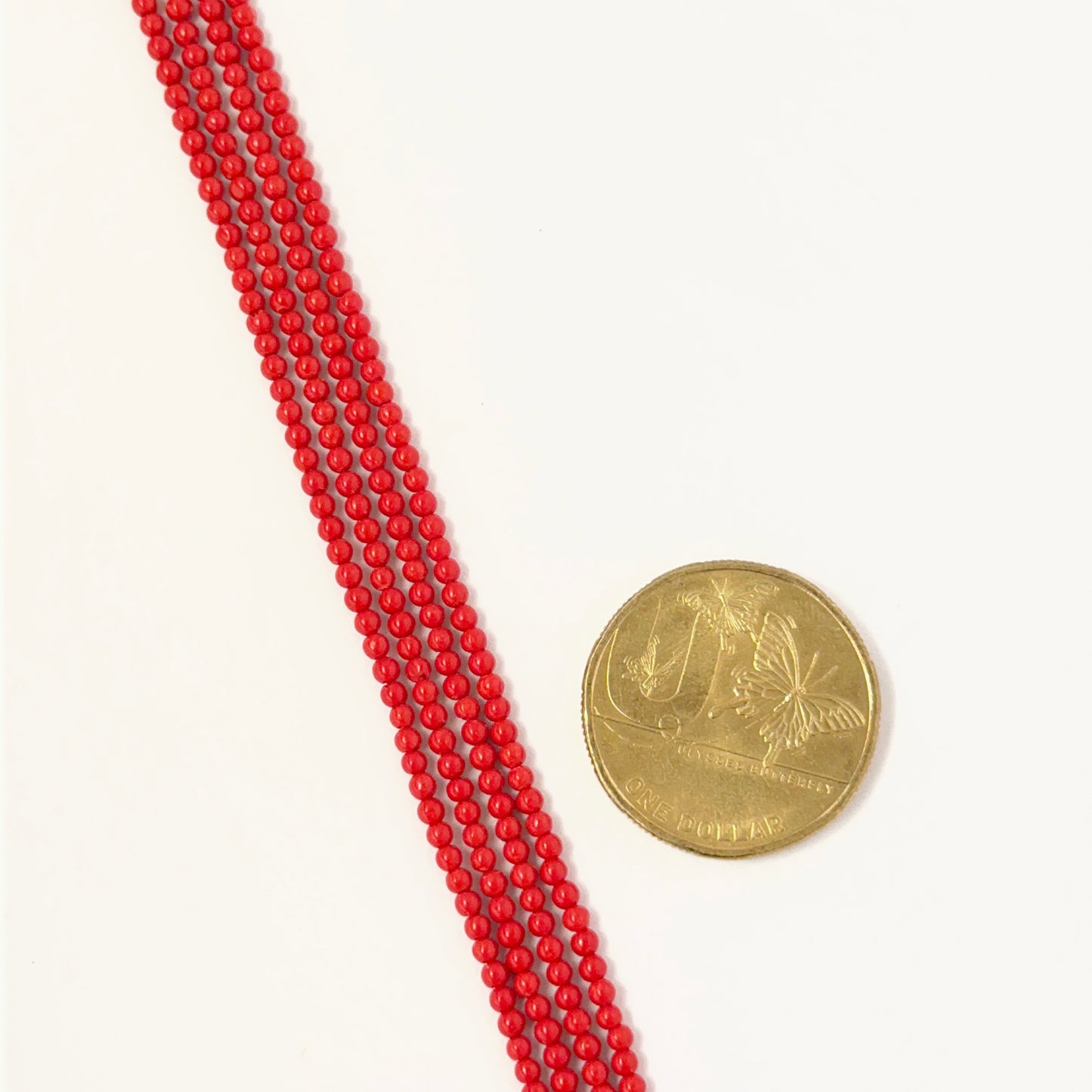 A coin placed next to Taiwan Coral smooth round beads strands for scale.