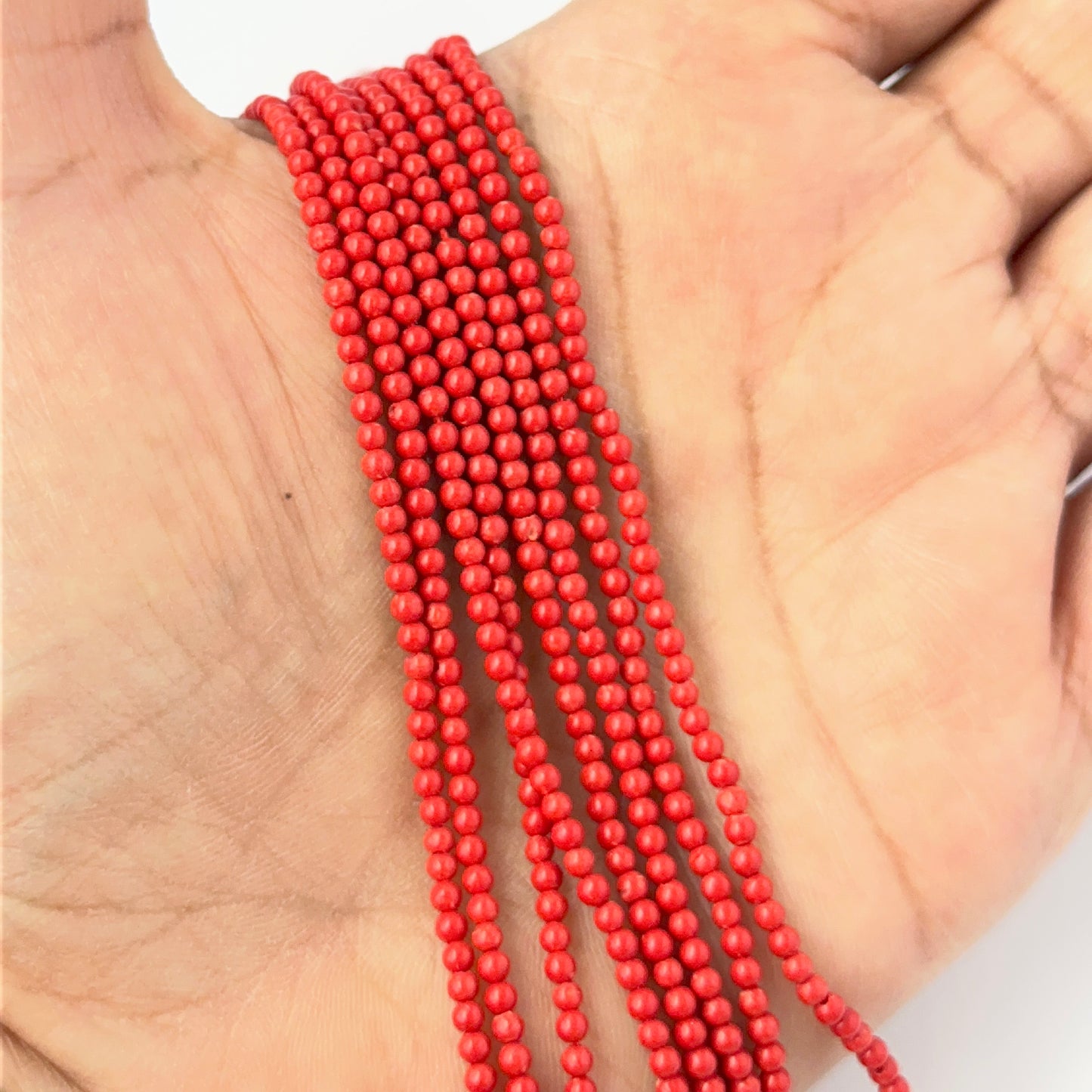 A person holds delicate strands of Taiwan Coral beads, showcasing their smooth design.