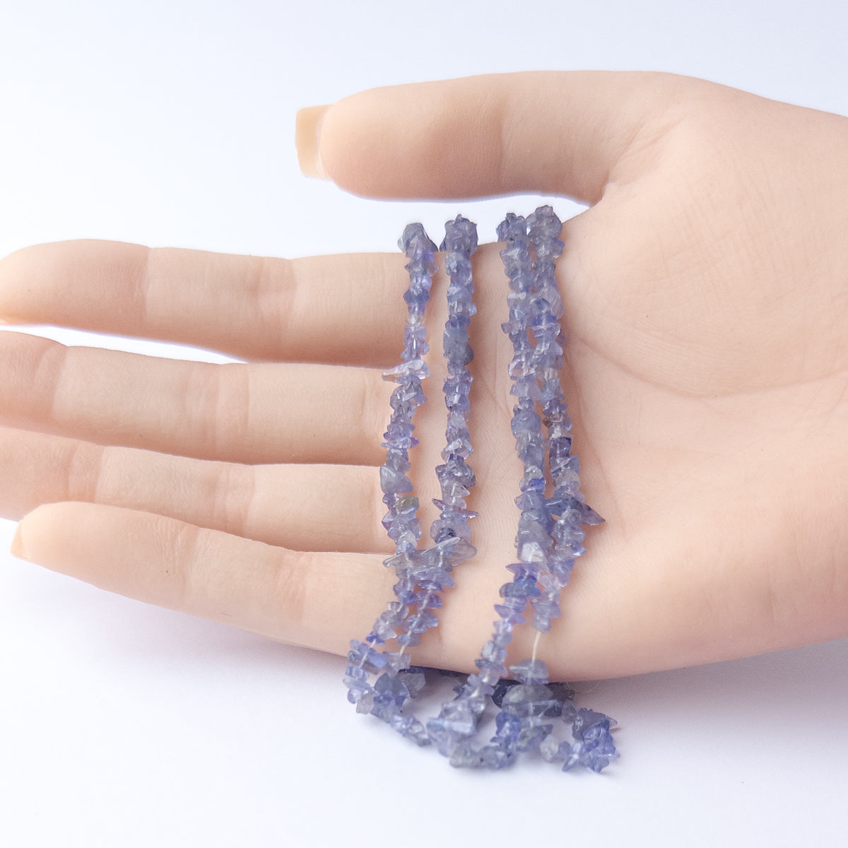 A person holds delicate strands of Tanzanite beads, showcasing their chip design.