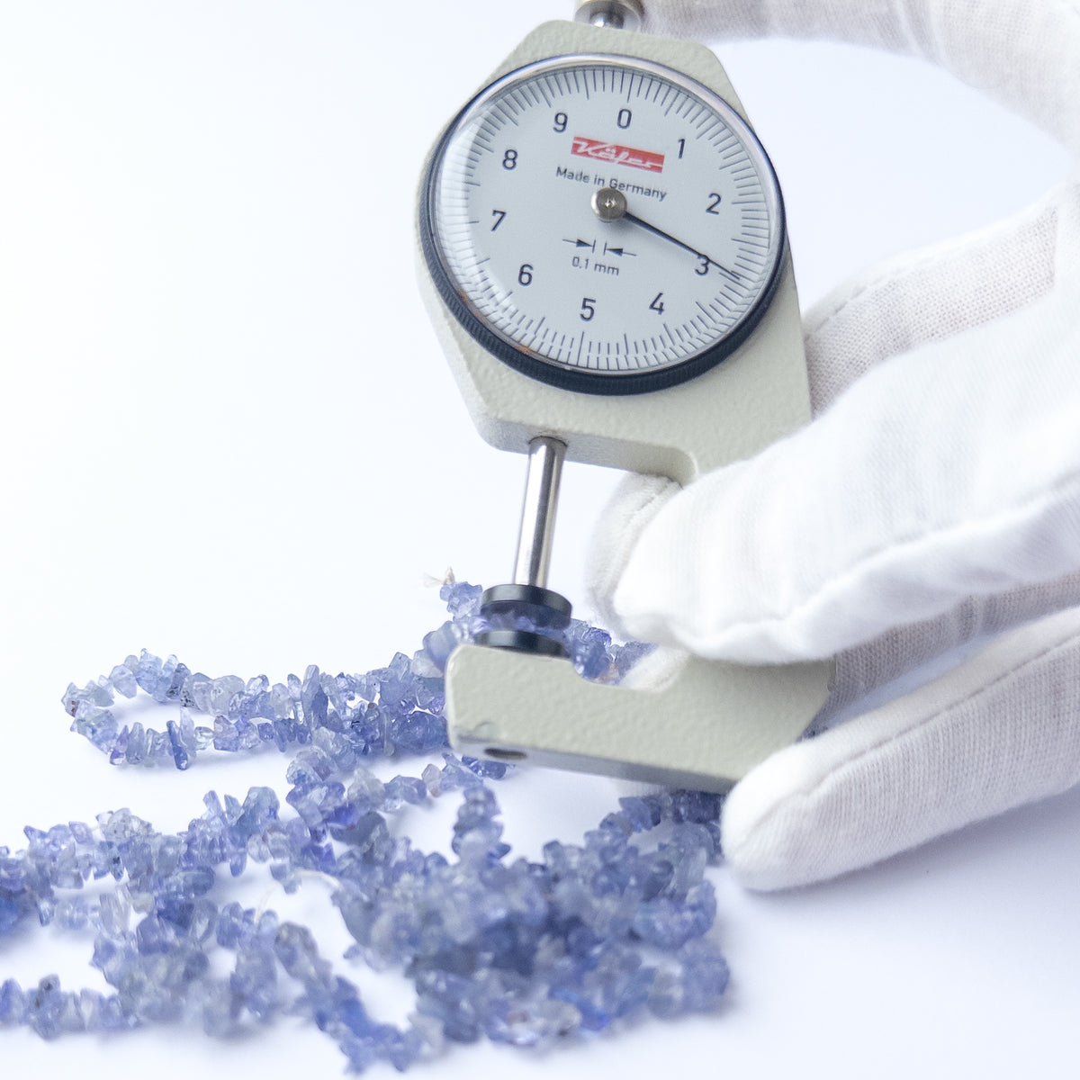 A dial gauge measures the Tanzanite chip 3–4mm gemstone.