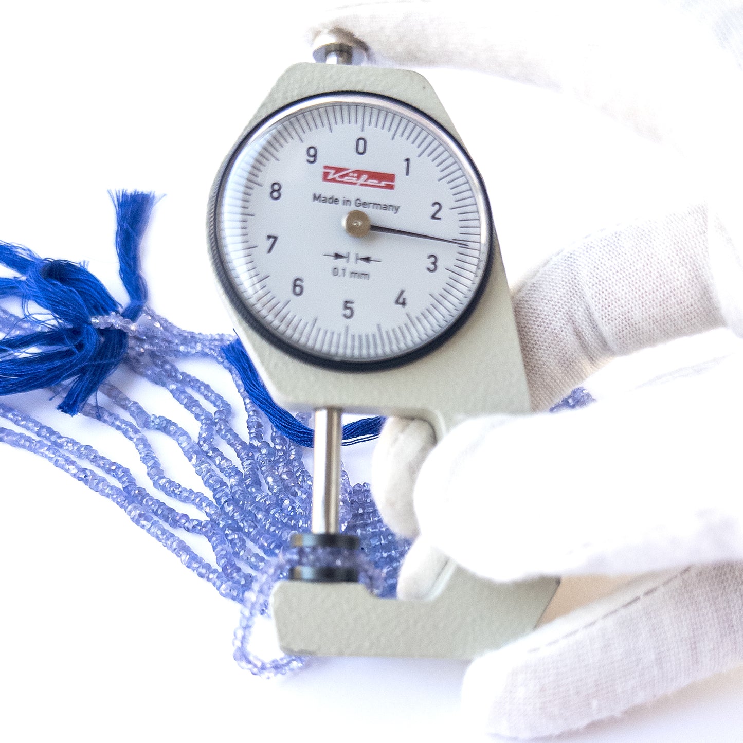 A dial gauge measures the Tanzanite faceted rondelle 2.6–3mm gemstone.