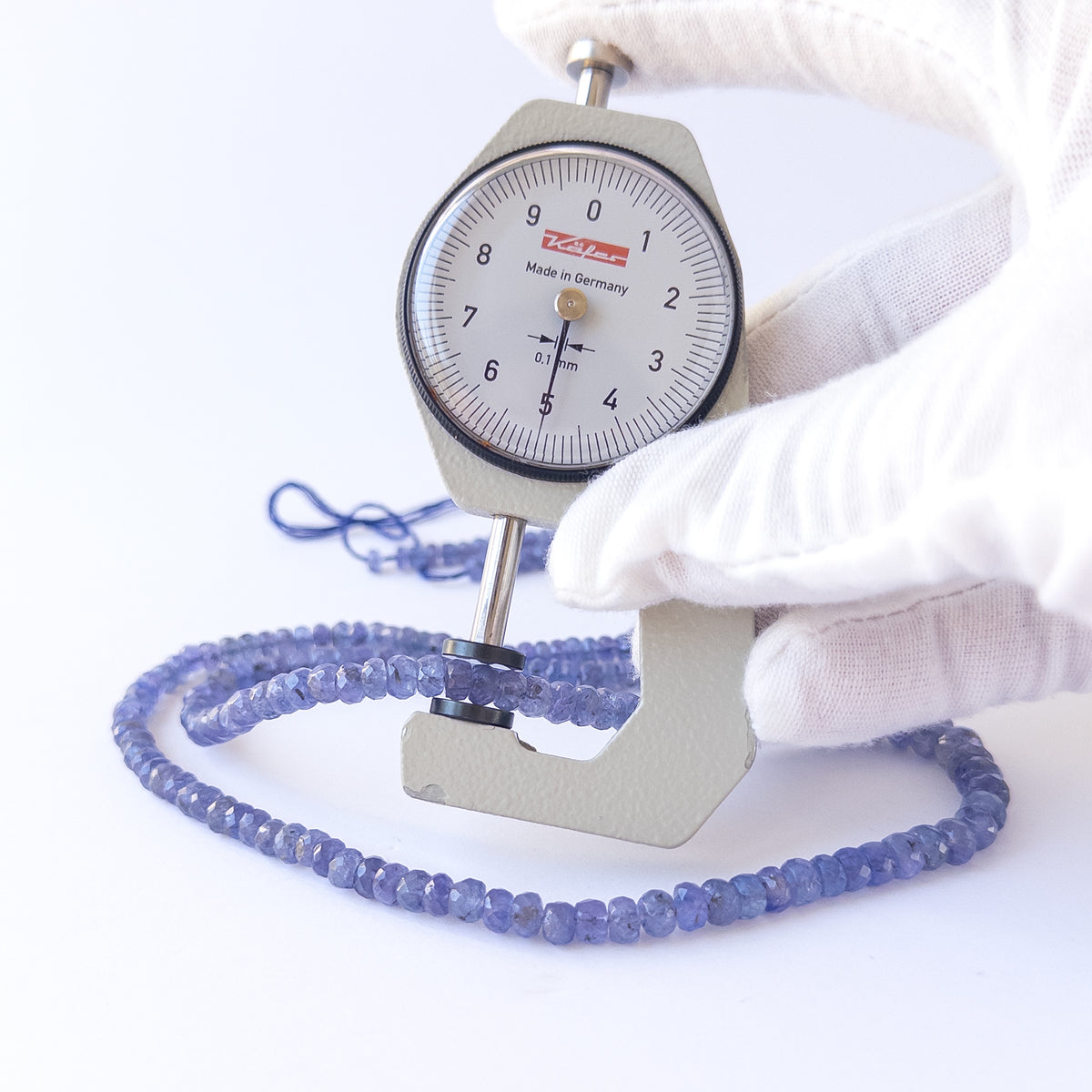 A dial gauge measures the Tanzanite faceted rondelle 4.1–6.2mm gemstone.