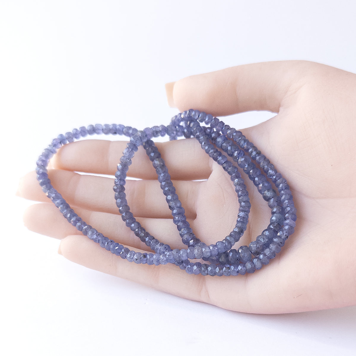 A person holds delicate strands of Tanzanite beads, showcasing their faceted rondelle design.