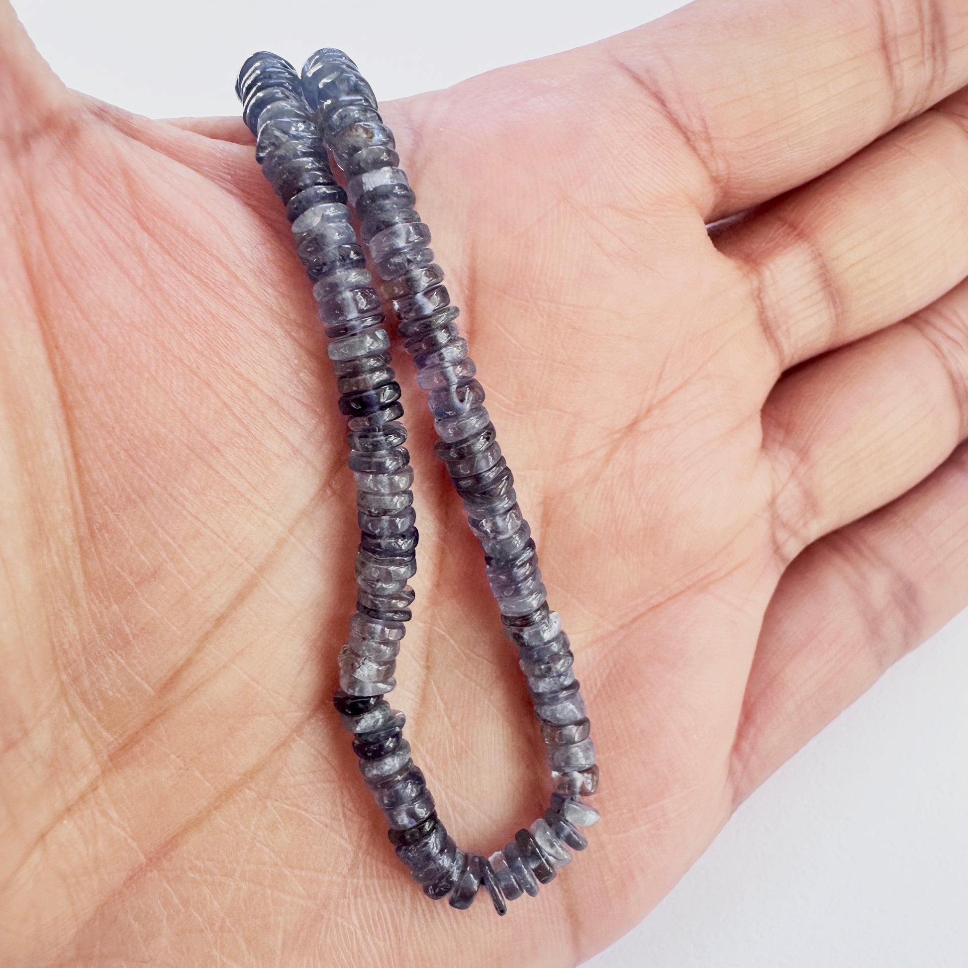 A person holds delicate strands of Tanzanite beads, showcasing their smooth design.