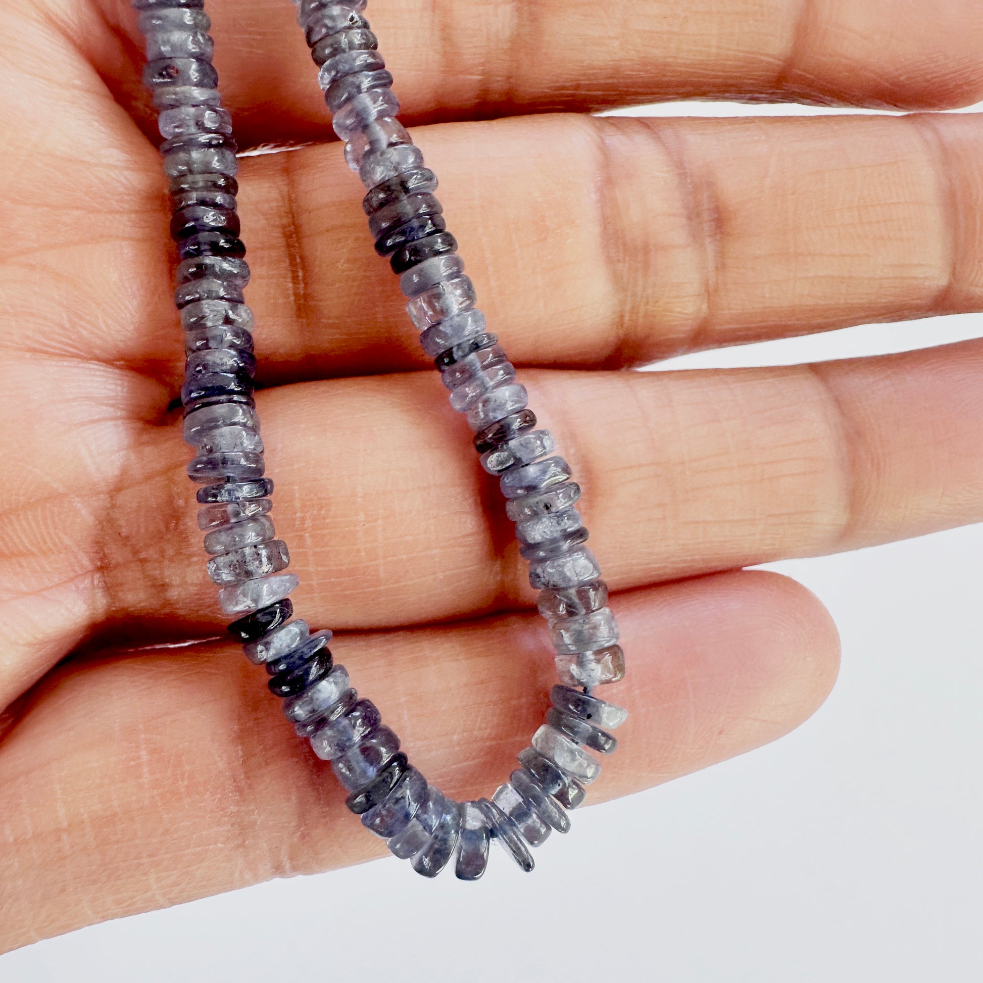 A person holds delicate strands of Tanzanite beads, showcasing their smooth design.