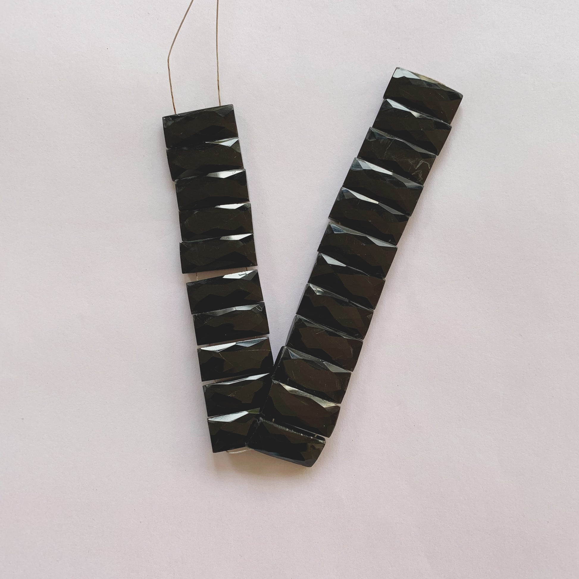 Jet-black faceted rectangle onyx beads in 20mm by 9mm size strung on a 20cm strand for jewellery making.