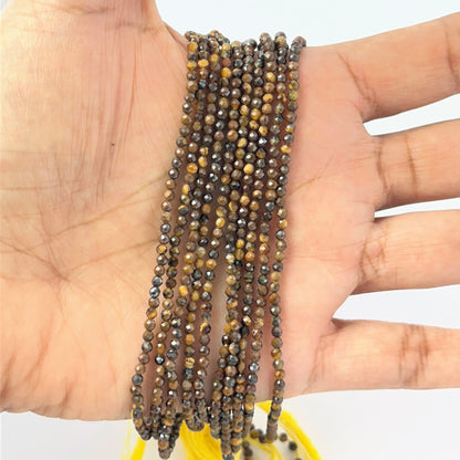 A person holds delicate strands of Tiger Eye beads, showcasing their faceted design.