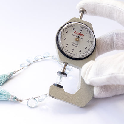 A dial gauge measures the Topaz faceted briolette 9.5–10mm gemstone.