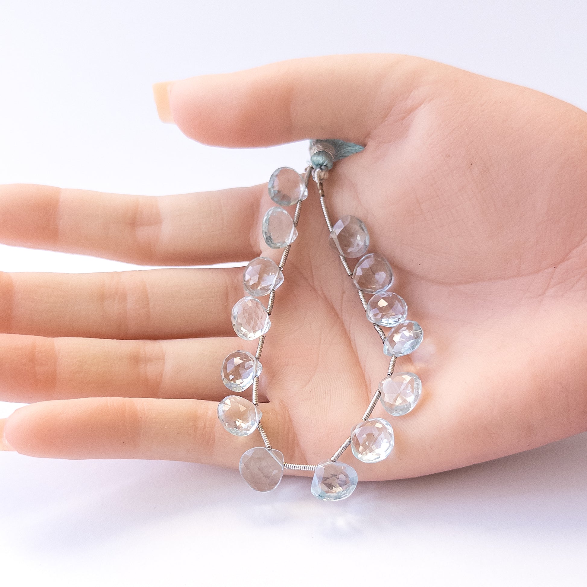 A person holds delicate pieces of Topaz beads, showcasing their faceted briolette design.