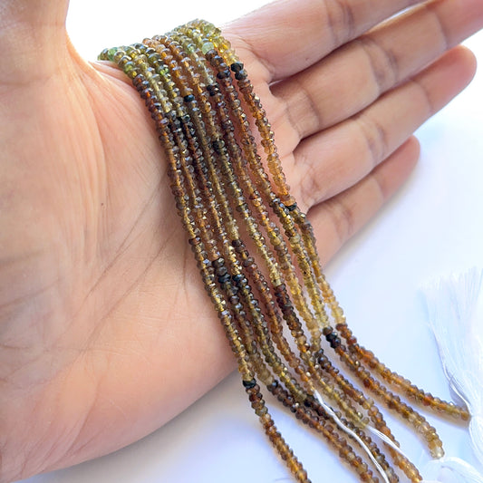 A person hand holding Tourmaline faceted rondelle 3–3.5mm beads on a 36cm strand displaying mixed pink and green hues for jewellery designers.