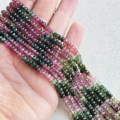 A person holds delicate strands of tourmaline beads, showcasing their faceted design.