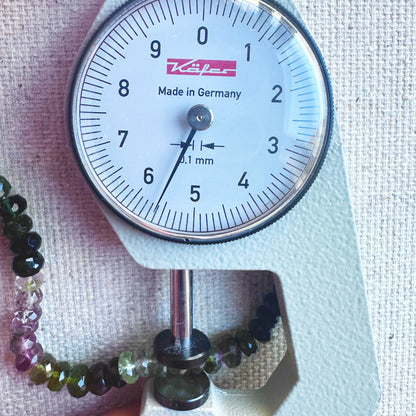 A dial gauge measures the tourmaline faceted rondelle 4.8mm–5.7mm gemstone for size accuracy.