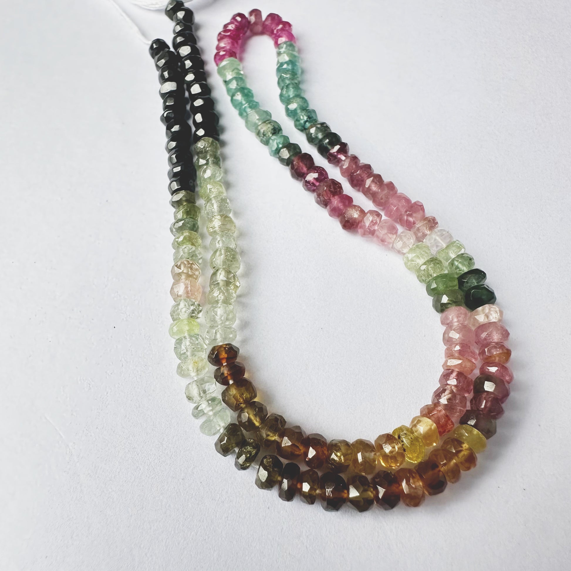Close-up of multi-coloured Tourmaline stone beads, faceted rondelle cut, sparkling under light.