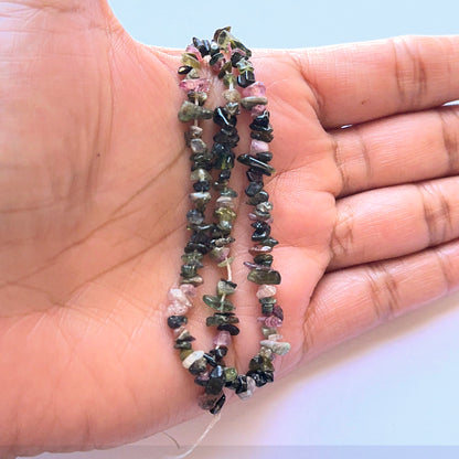 A person holds delicate strands of Tourmaline beads, showcasing their smooth design.