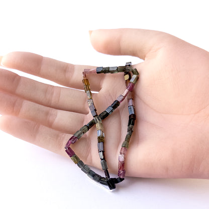 A person holds delicate strands of Tourmaline smooth rectangle beads, showcasing their polished design.