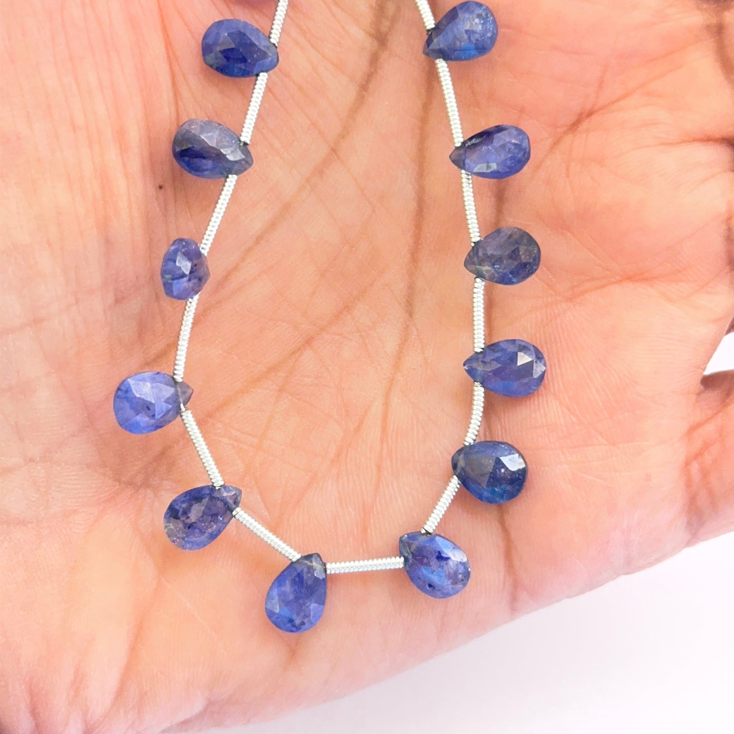 A person holds the Blue Sapphire pear faceted almond bead set, showcasing the top side drilled holes and rich blue tones.
