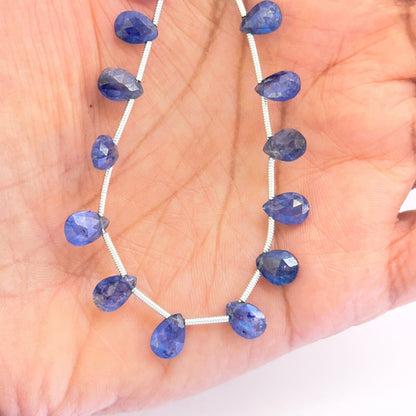 A person holds the Blue Sapphire pear faceted almond bead set, showcasing the top side drilled holes and rich blue tones.

