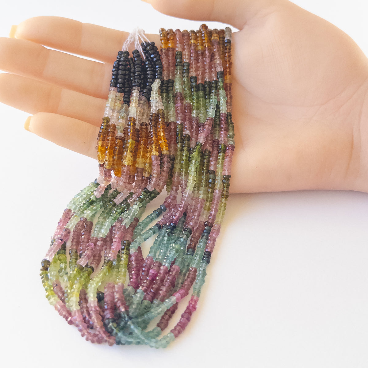 A person holds delicate strands of Watermelon Tourmaline beads, showcasing their faceted rondelle design.