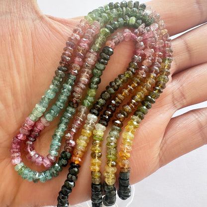 A person holds delicate strands of Watermelon Tourmaline beads, showcasing their smooth design and vivid colour gradient.
