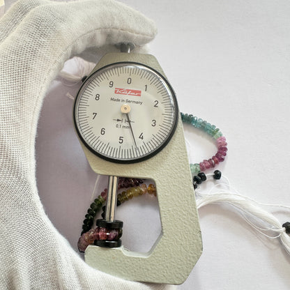 A dial gauge measures the Watermelon Tourmaline faceted rondelle 4.5mm gemstone, ensuring accurate bead sizing.