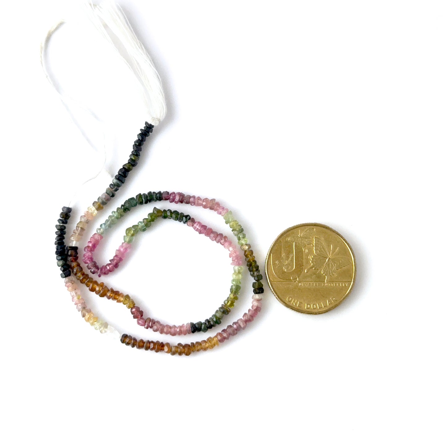 A coin is placed near delicate strands of Watermelon Tourmaline beads for scale.