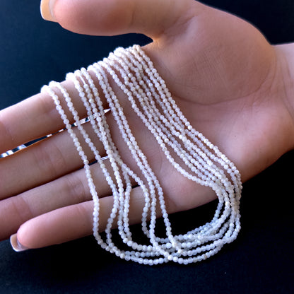 A person holds delicate strands of White Opal beads, showcasing their faceted rondelle design.