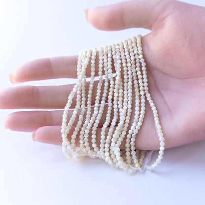 A person holds delicate strands of White Opal beads, showcasing their faceted rondelle design.
